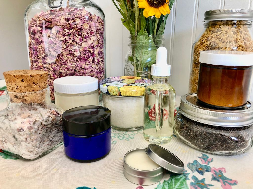 Image of oils, butters, balms, and herbs in glass bottles and jars. Sustainable, reusable packaging to reduce plastic waste. 